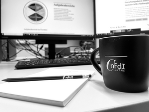 Cup, pencil and notepad on desk in front of monitors