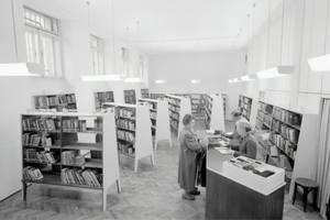 A library user stands across from two library staff members at a counter. 