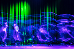 ca. 16 schattenhafte Tänzer in violett und blau vor einem abstrakten grün-schwarzen Hintergrund